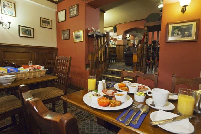 Cozy dining area with wooden chairs, a table set with a full English breakfast, and warm lighting.