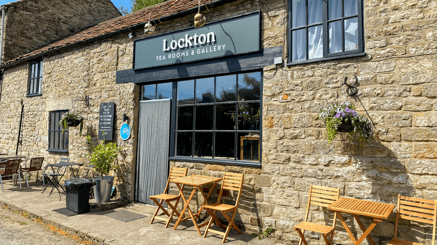 Quaint stone building with a sign reading "Lockton Tea Rooms & Gallery," featuring outdoor seating and hanging plants.